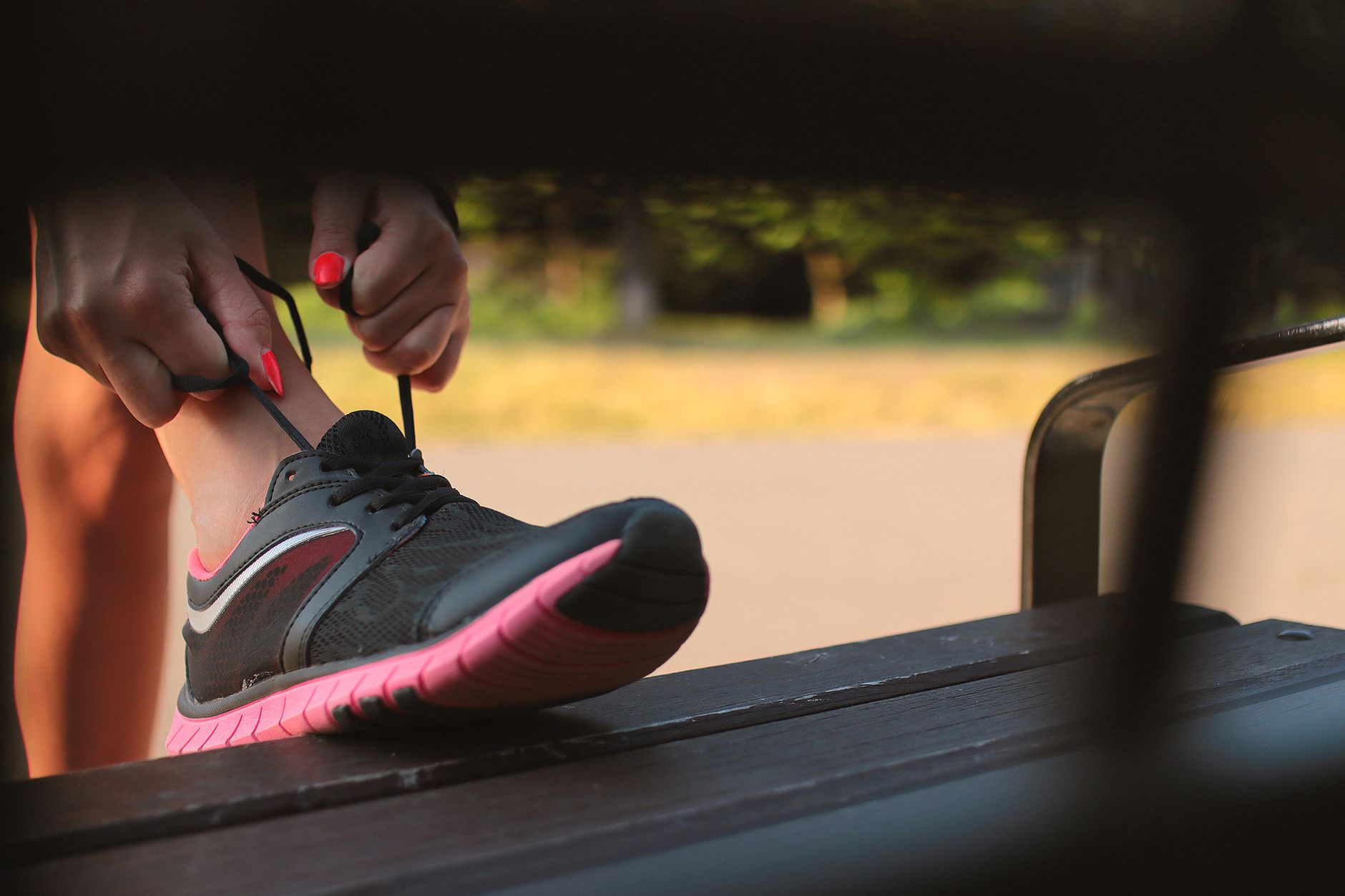 Femme laçant sa chaussure de course assise sur un banc en extérieur