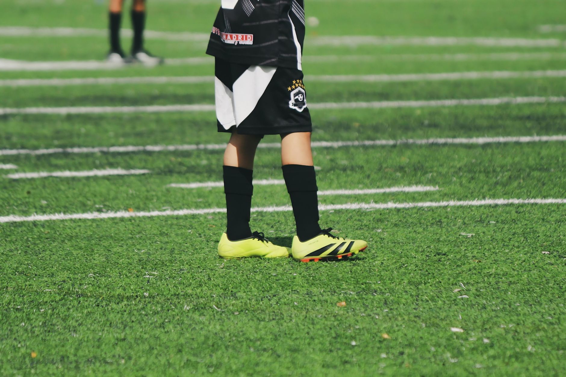 Jambes d’un enfant en tenue de football sur un terrain synthétique